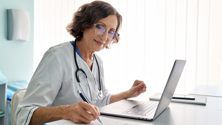 Doctor using laptop and writing